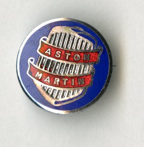 Lapel pin with 'Aston Martin' on a ribbon around pre-war grille, dated c.1948-1950.